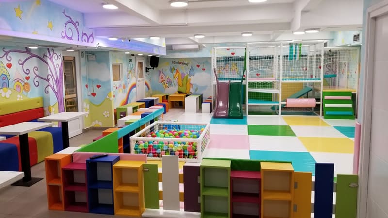 Bazen sa lopticama ograđen niskim policama u boji, lavirint sa toboganima u pozadini