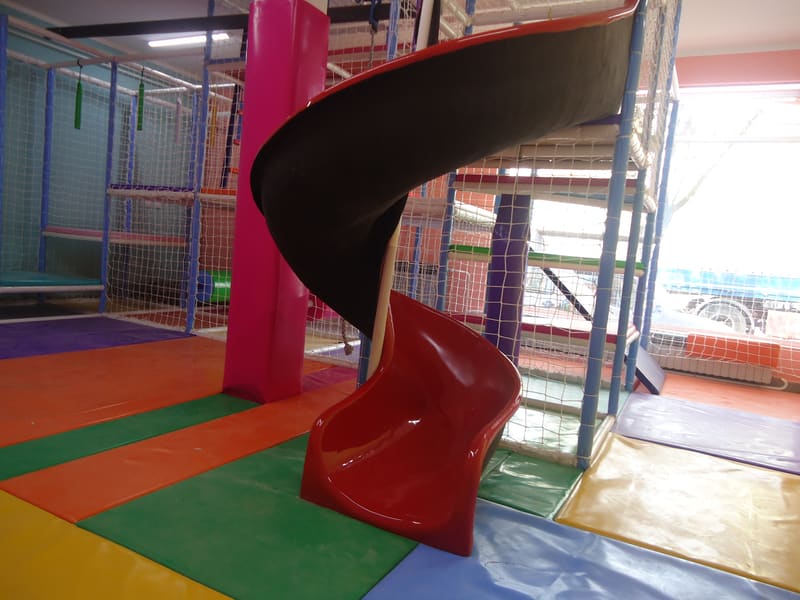 Crveni spiralni tobogan na šarenim mekim podlogama, lavirint u pozadini